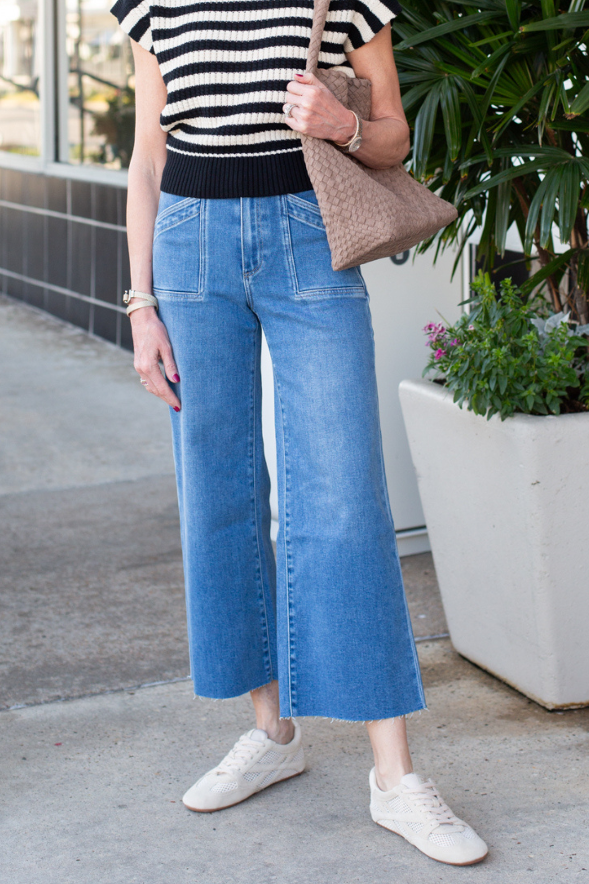 Person wearing a striped shirt, blue jeans, and white sneakers standing outdoors.
