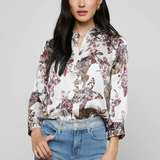 Woman wearing a floral blouse and blue jeans against a gray background