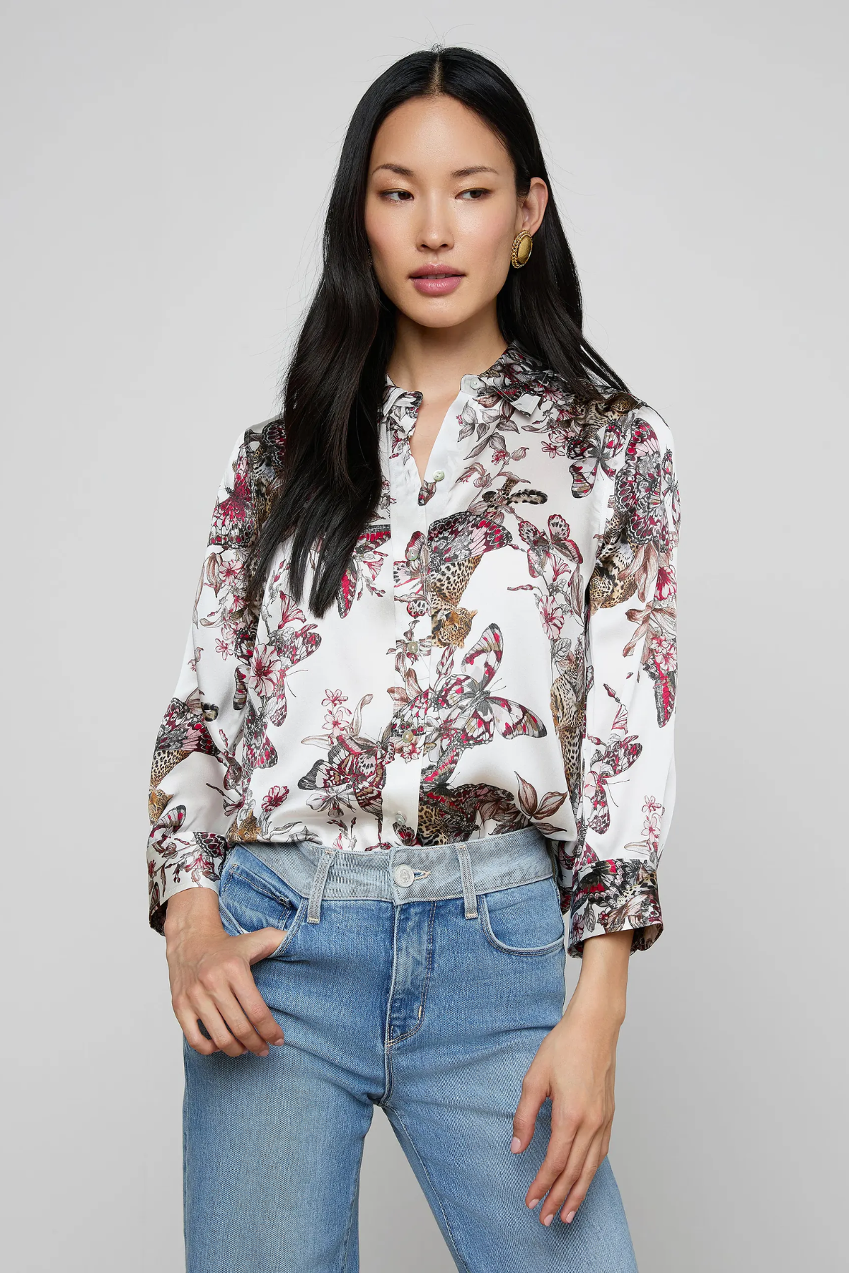 Woman wearing a floral blouse and blue jeans against a gray background