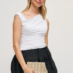 Woman wearing a white sleeveless top and black skirt, holding a beige clutch against a plain background
