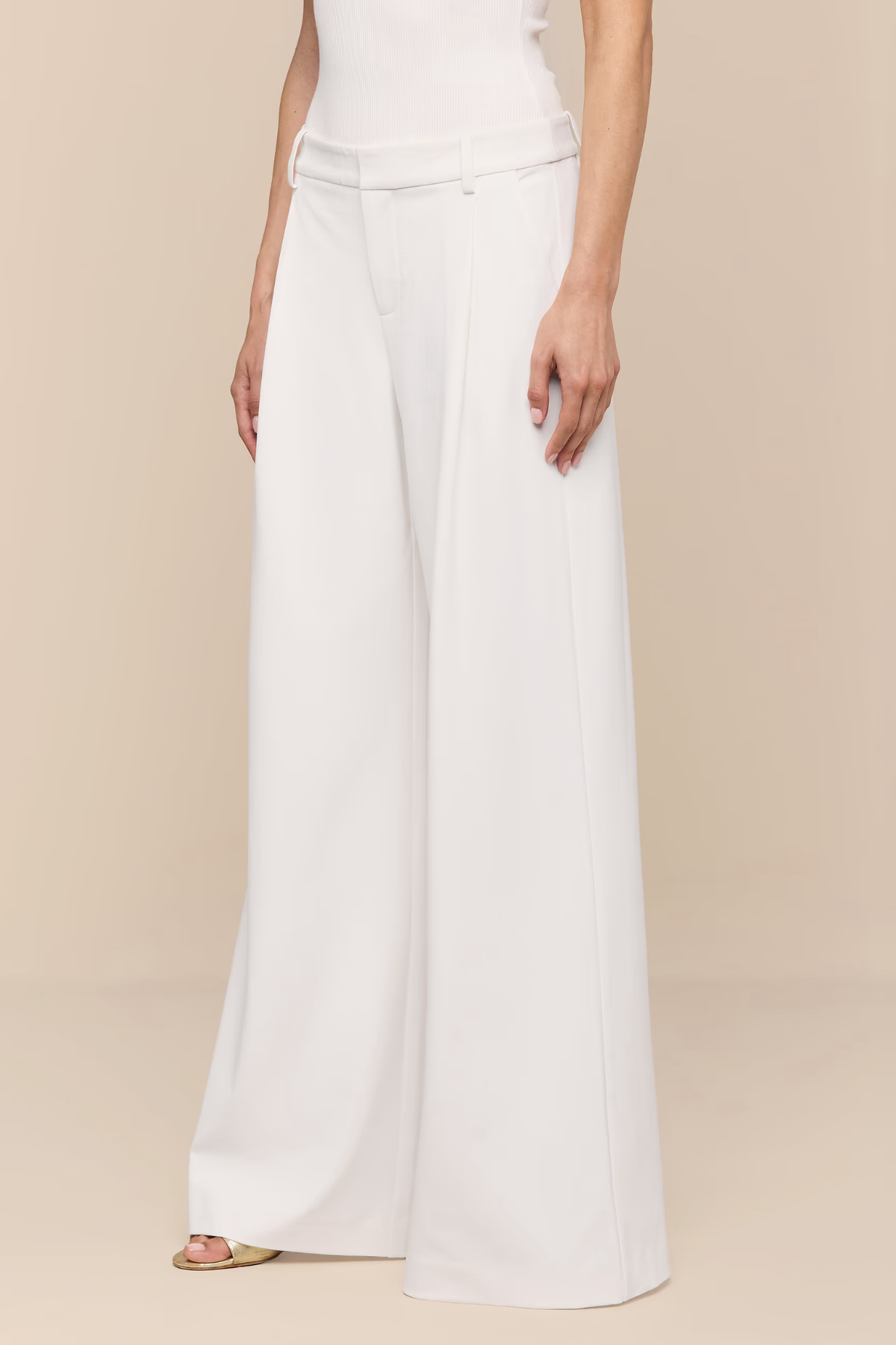 Person wearing white wide-leg pants on a beige background