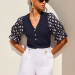 Woman wearing a navy floral blouse and white shorts against a beige wall.