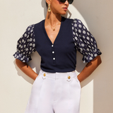 Woman wearing a navy floral blouse and white shorts against a beige wall.