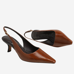 A pair of brown leather slingback pumps with pointed toes and kitten heels, displayed against a light gray background.