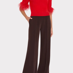 A model wearing a vibrant red mock-neck top with feathered elbow-length sleeves and dark brown wide-leg trousers, shown against a light gray studio background.