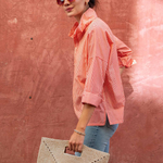 side view of woman in striped button down shirt standing by brick wall 