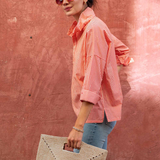 side view of woman in striped button down shirt standing by brick wall 