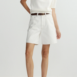 Person wearing a white top and shorts with a belt on a plain background