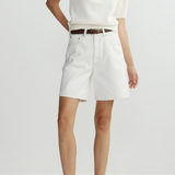 Person wearing a white top and shorts with a belt on a plain background