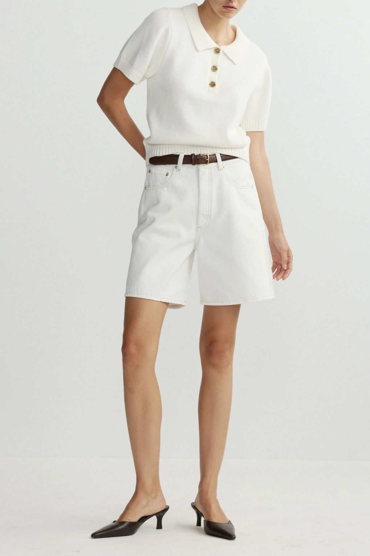 Person wearing a white top and shorts with a belt on a plain background