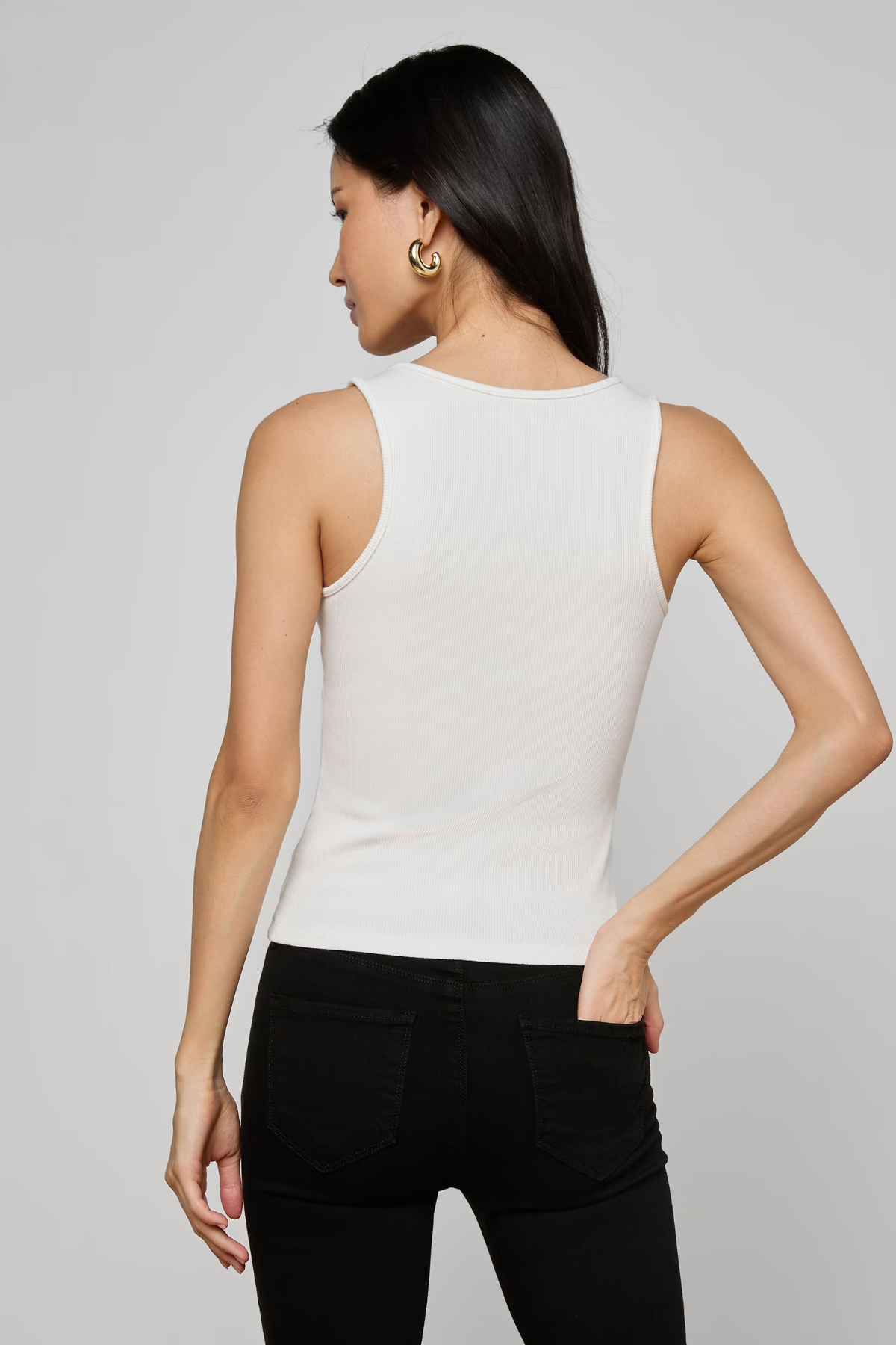 Woman wearing a white sleeveless top and black pants on a gray background