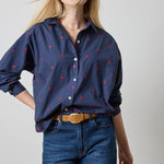 Woman wearing a navy blue shirt with red patterns and blue jeans on a plain background
