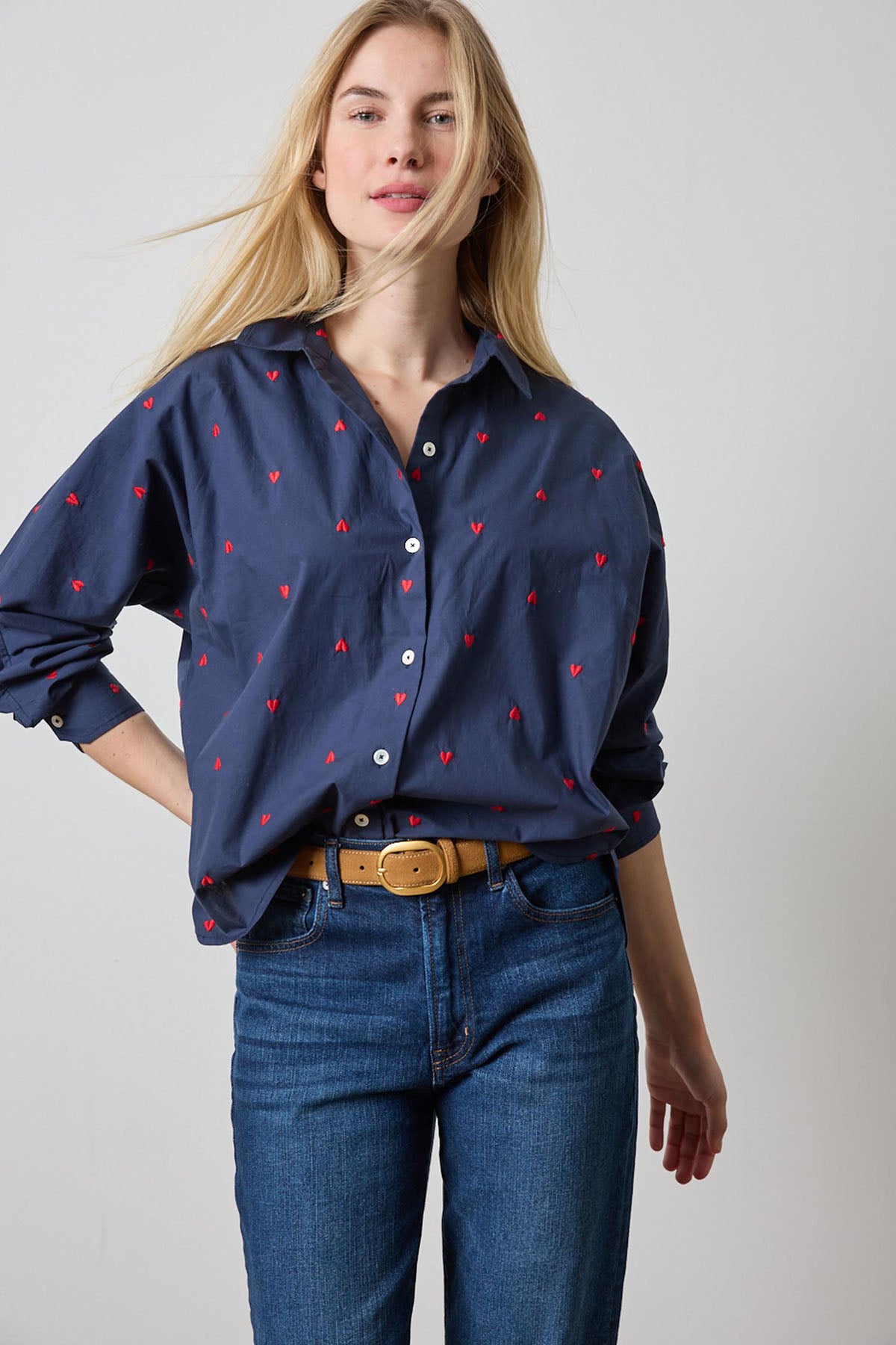 Woman wearing a navy blue shirt with red patterns and blue jeans on a plain background