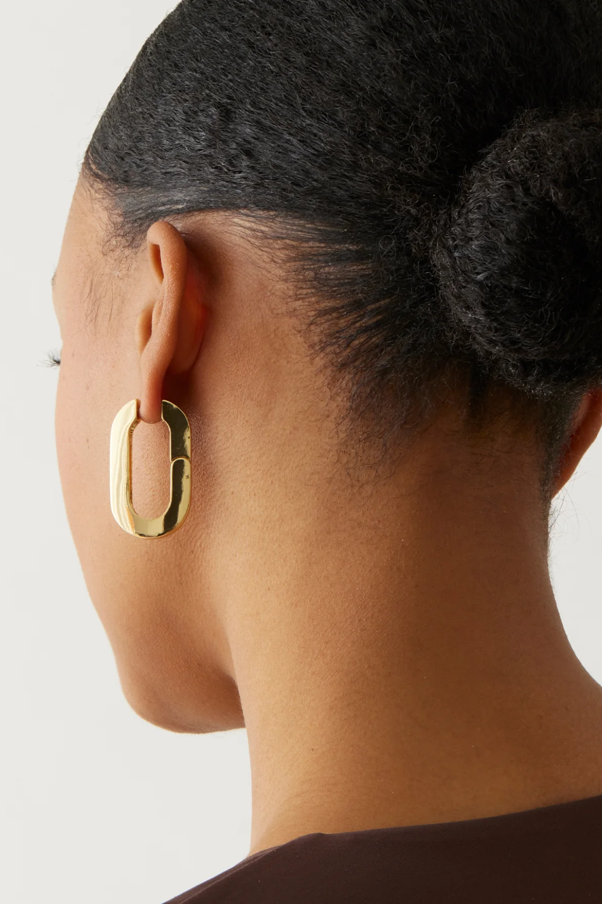 Gold hoop earring worn by a person with a neutral background