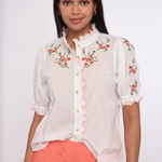 Woman wearing a white blouse with floral embroidery and a coral skirt on a white background