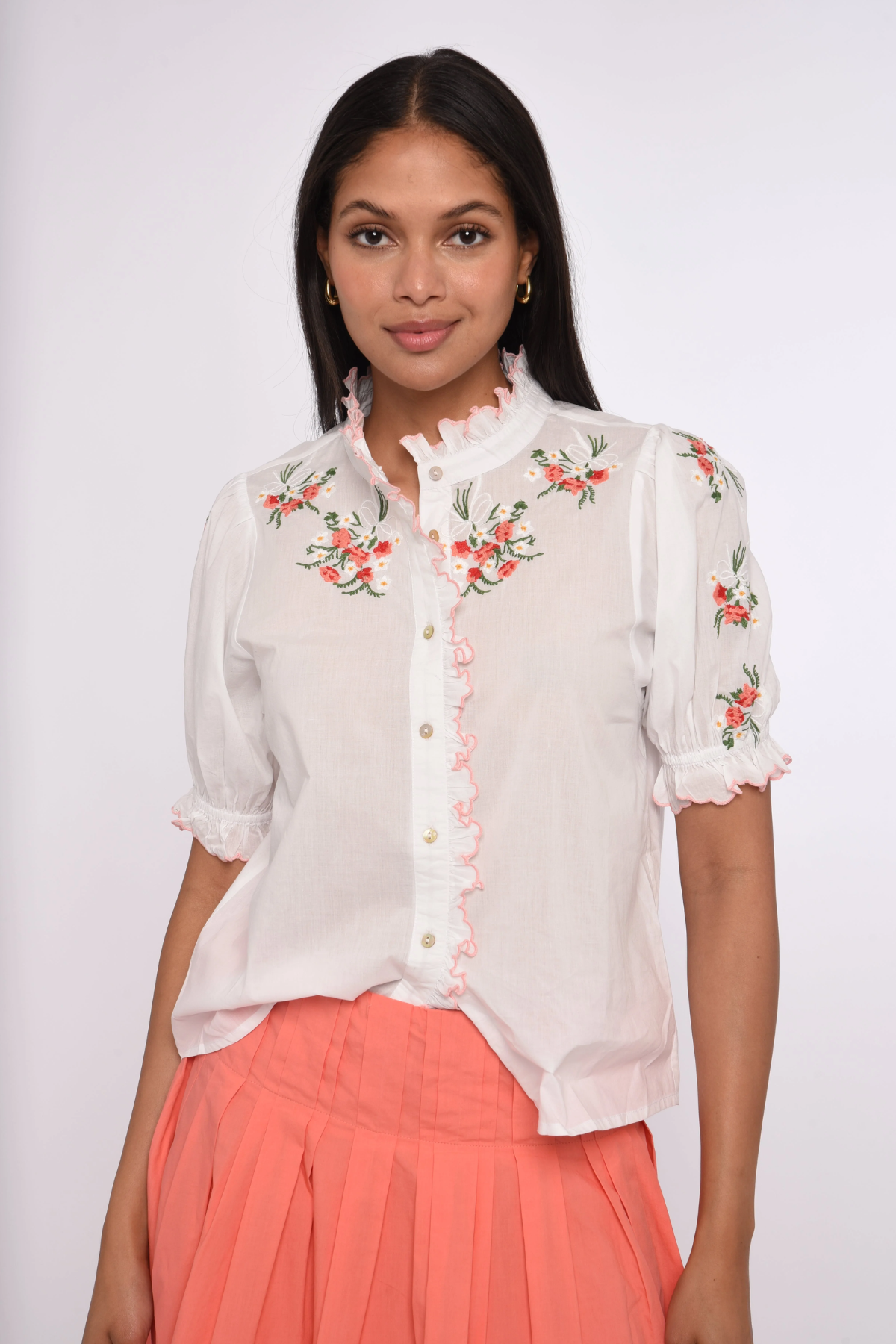 Woman wearing a white blouse with floral embroidery and a coral skirt on a white background
