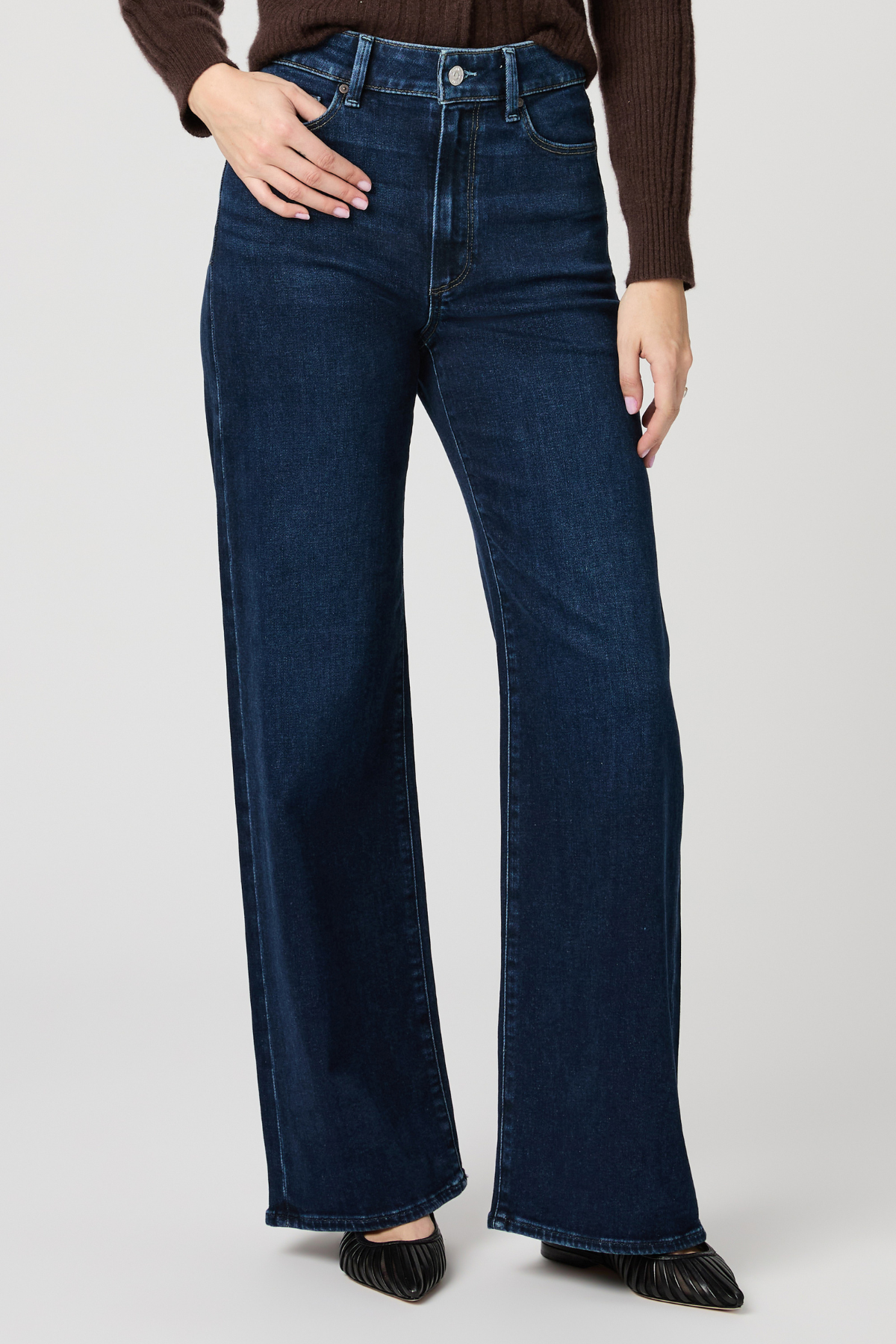 Person wearing dark blue jeans on a plain background