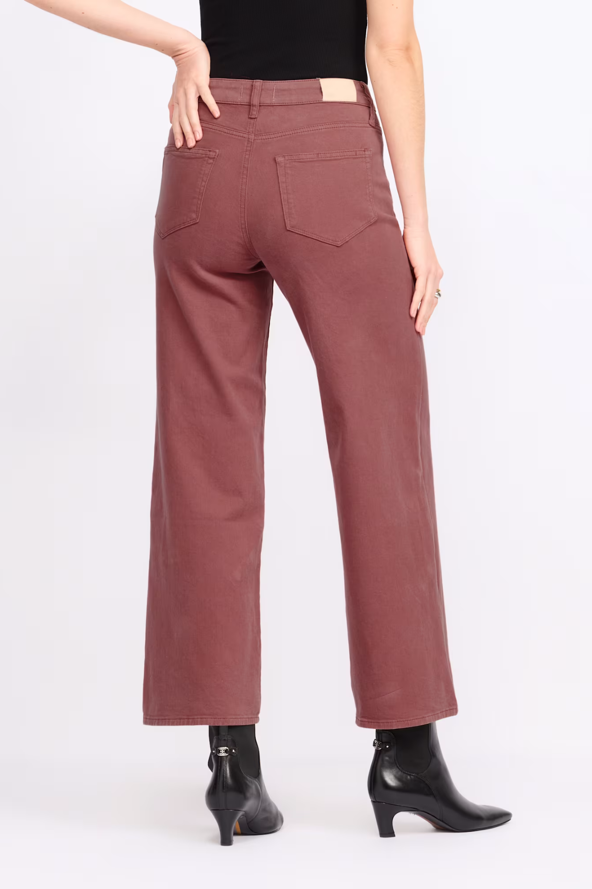 A person shown from the back wearing dusty rose wide-leg cropped pants with black ankle boots against a plain light gray studio background.