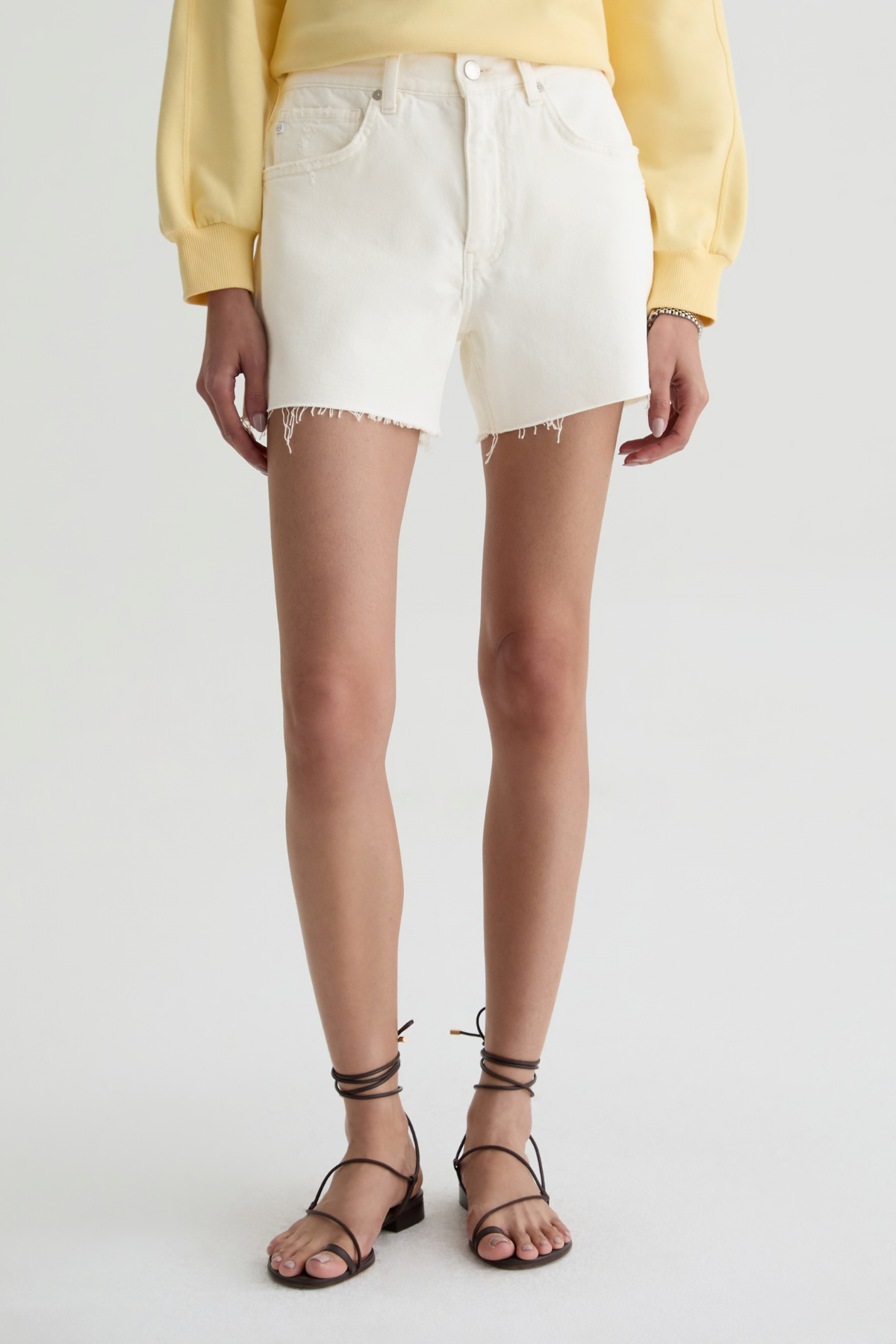 Person wearing a yellow top and white denim shorts on a plain background