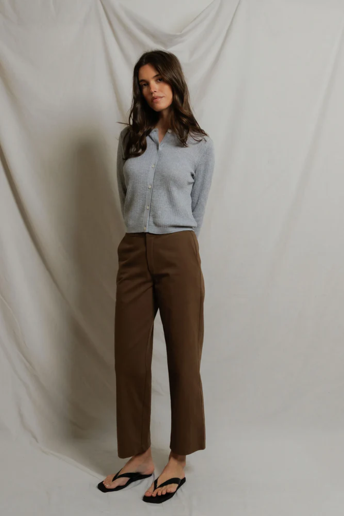 woman in grey cardigan and brown pants on draped background 