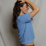 side view of woman in blue top on tan background 