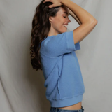 side view of woman in blue top on tan background 