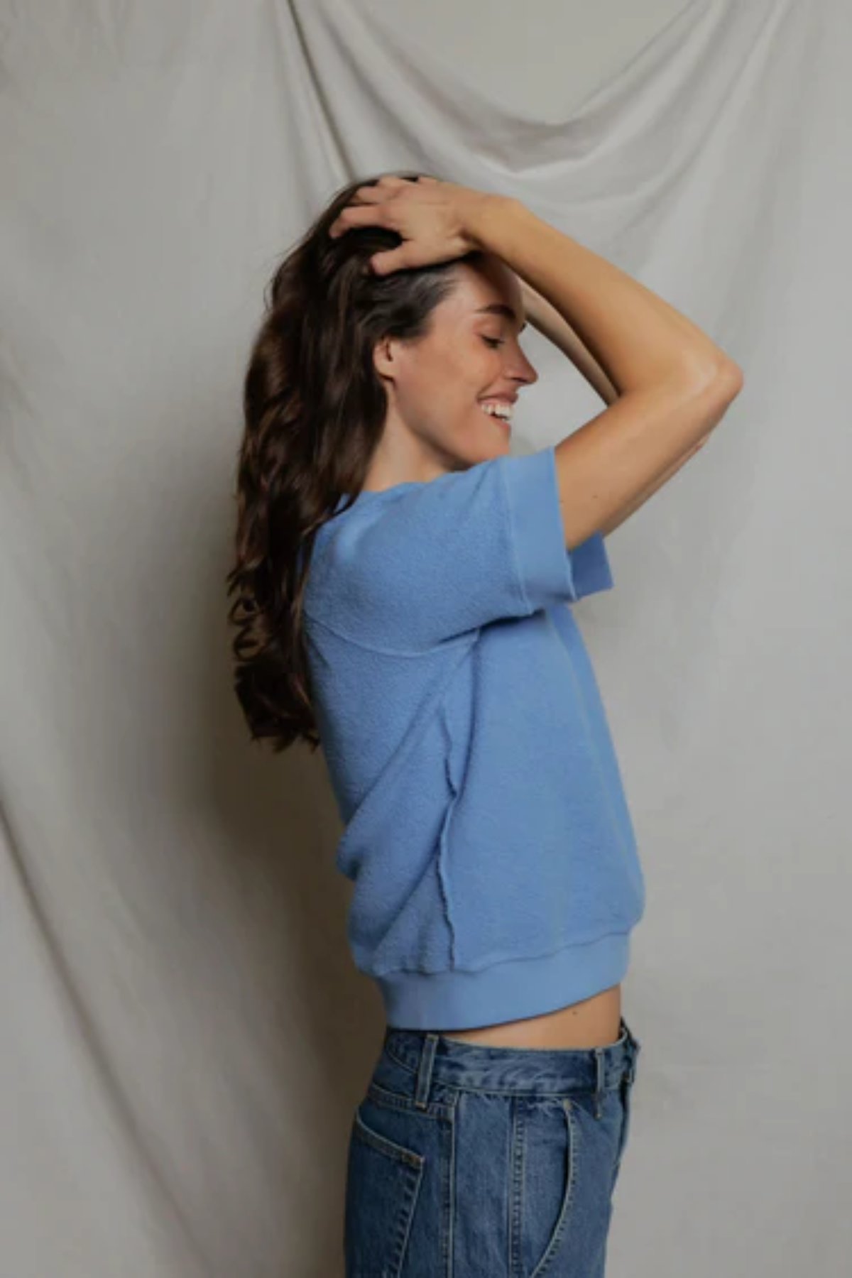 side view of woman in blue top on tan background 