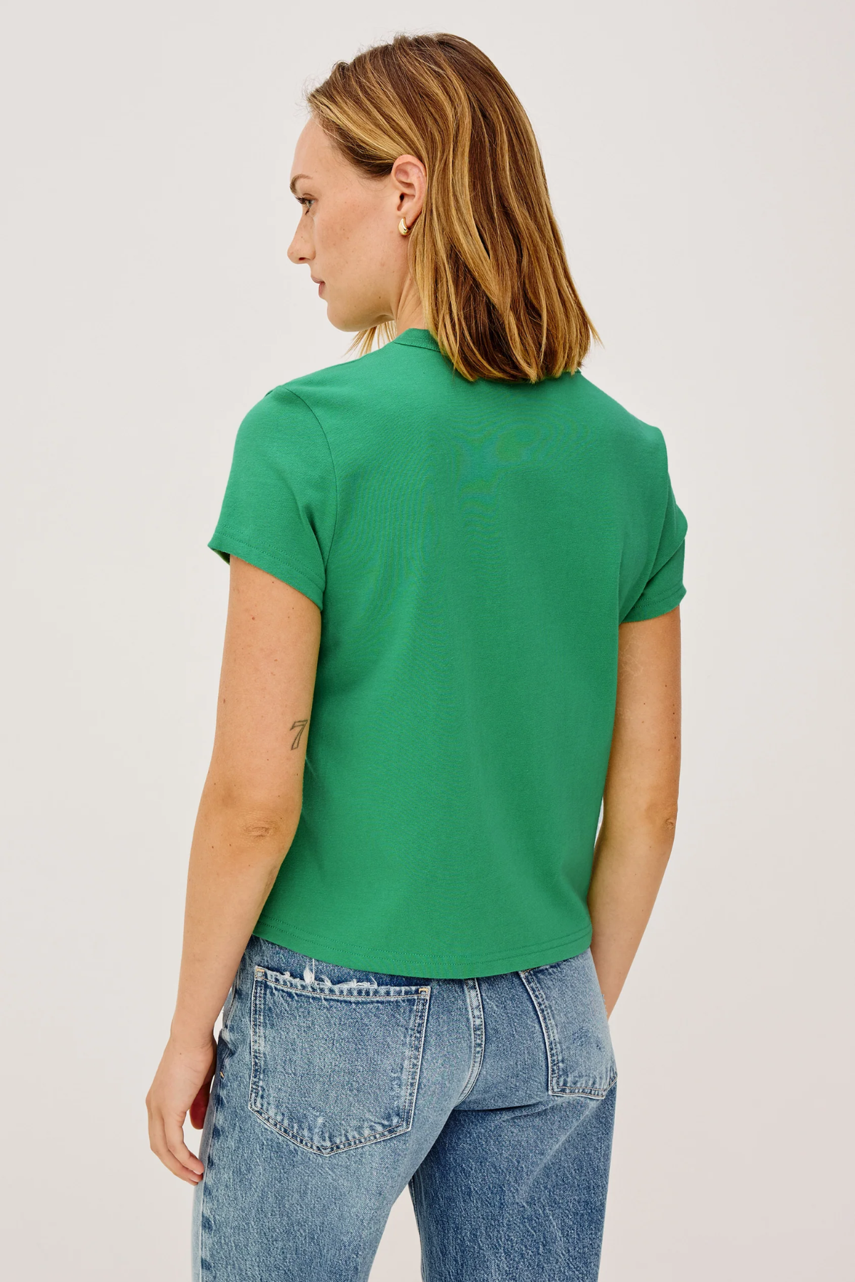 Person wearing a green t-shirt and blue jeans on a plain background
