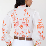 Woman wearing a white blouse with orange floral and bird patterns on a plain background