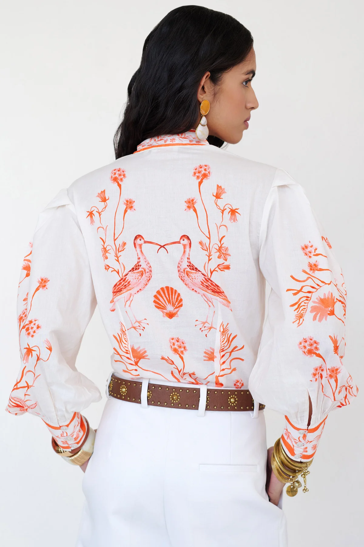 Woman wearing a white blouse with orange floral and bird patterns on a plain background