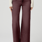 A model wearing a pair of wide-leg, high-waisted jeans in a washed plum or burgundy shade, styled with a cream ribbed knit sweater and beige pointed-toe heels against a light gray studio background.