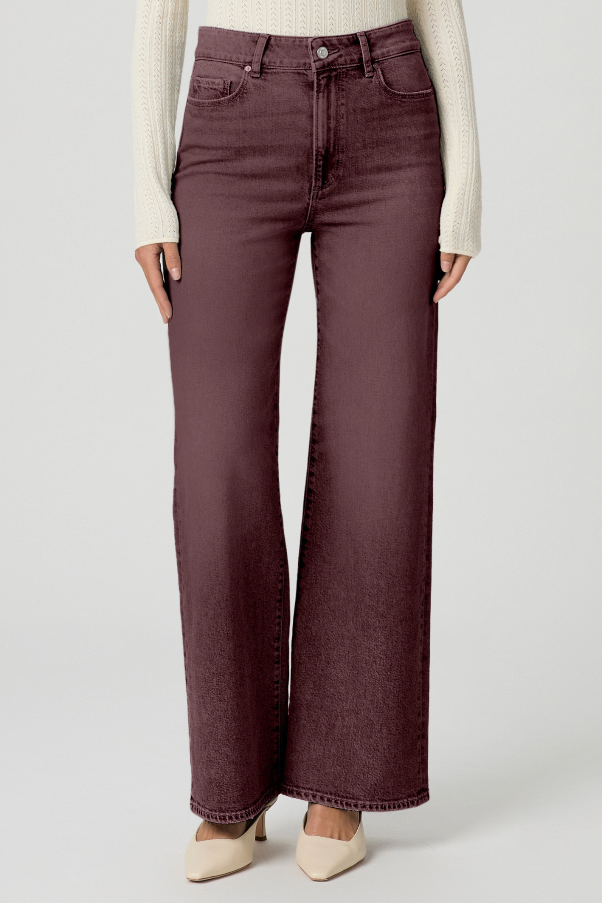 A model wearing a pair of wide-leg, high-waisted jeans in a washed plum or burgundy shade, styled with a cream ribbed knit sweater and beige pointed-toe heels against a light gray studio background.