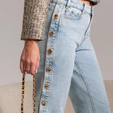 Light blue jeans with gold buttons worn by a person, holding a black handbag.