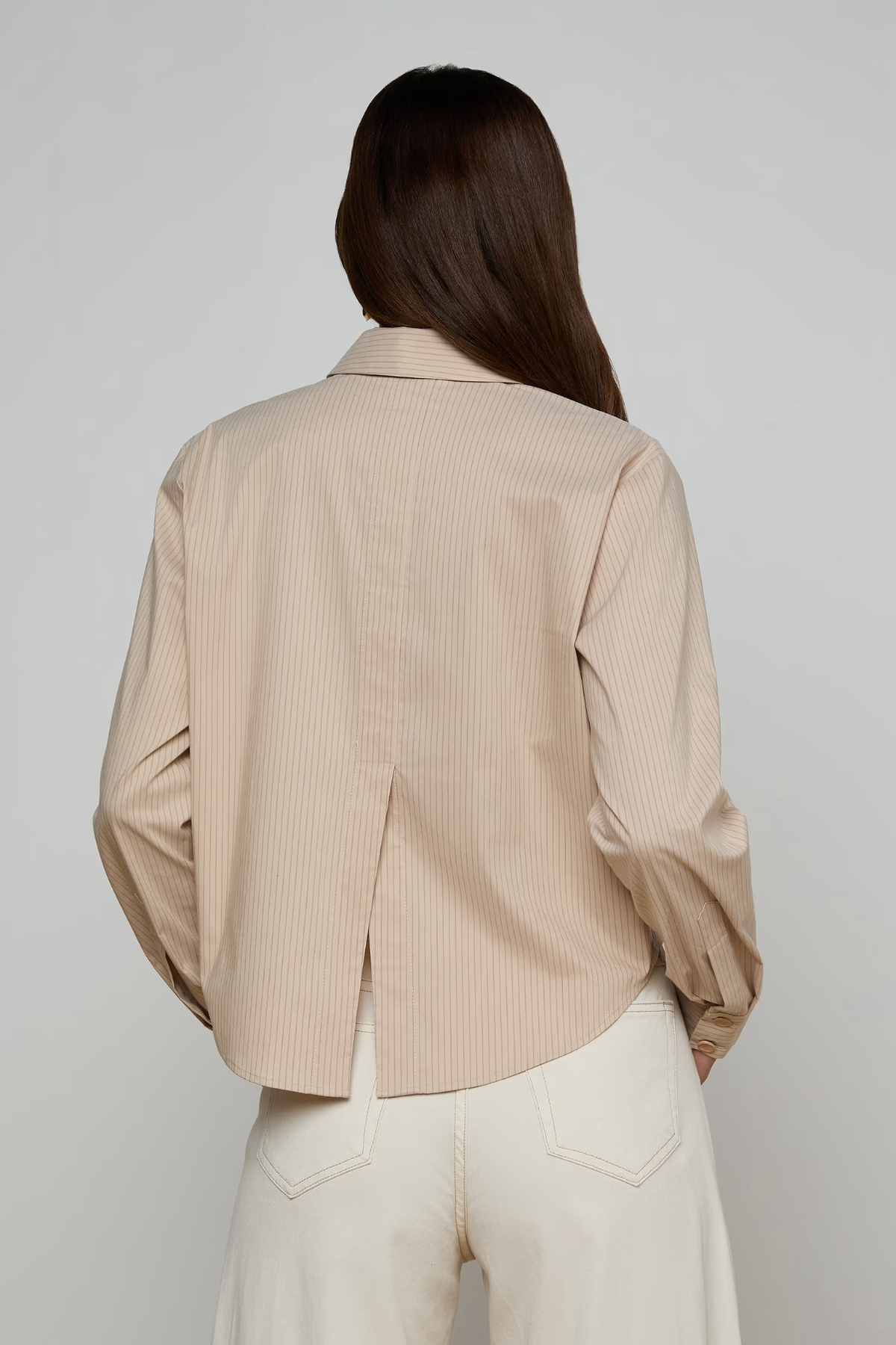 Woman wearing a beige ribbed blouse against a plain background
