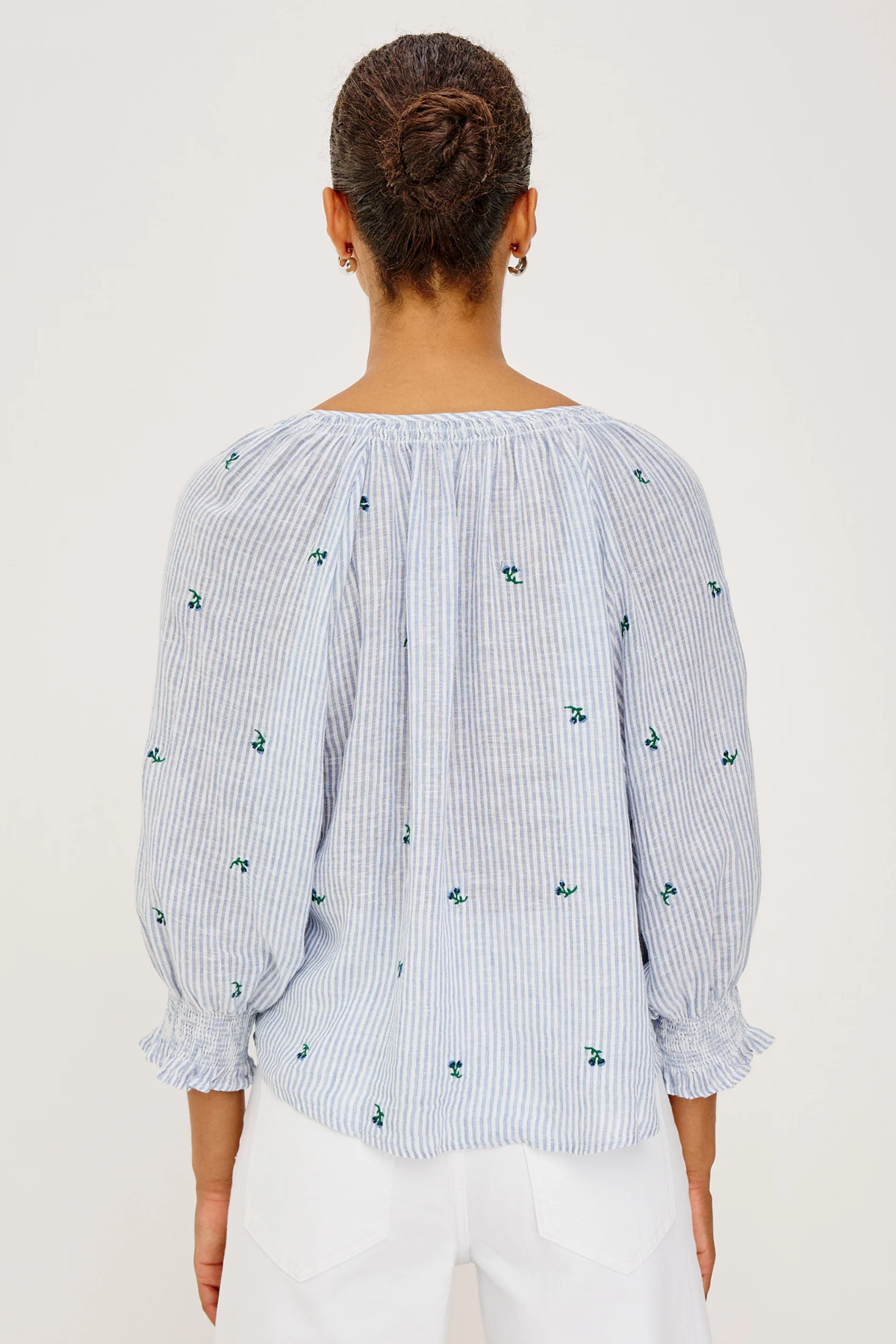 Woman wearing a light blue striped blouse with floral patterns on a white background