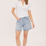 A woman modeling a white short-sleeve polo shirt and light-wash denim shorts against a plain light background.