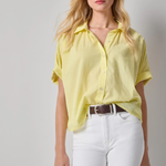 Woman wearing a yellow shirt and white pants against a gray background