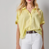 Woman wearing a yellow shirt and white pants against a gray background