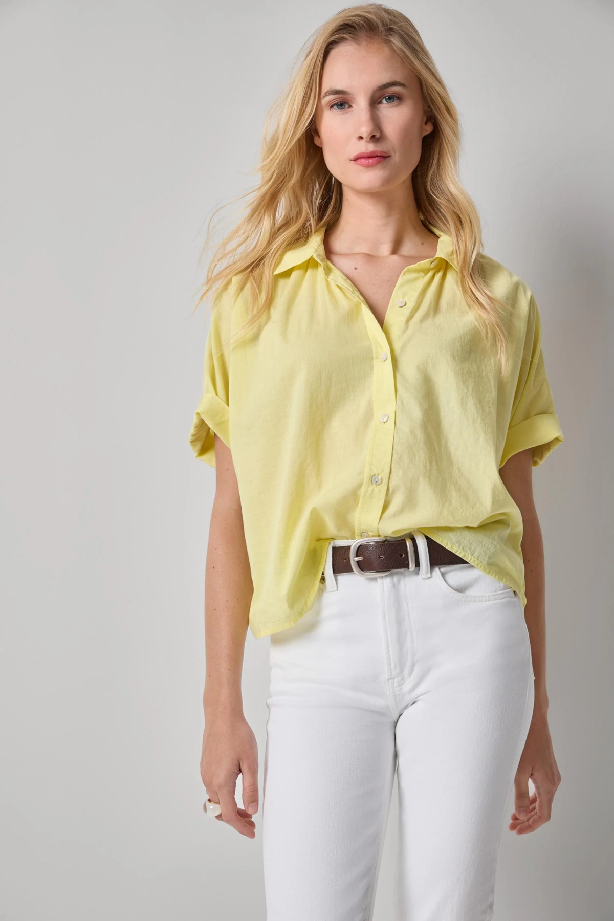 Woman wearing a yellow shirt and white pants against a gray background