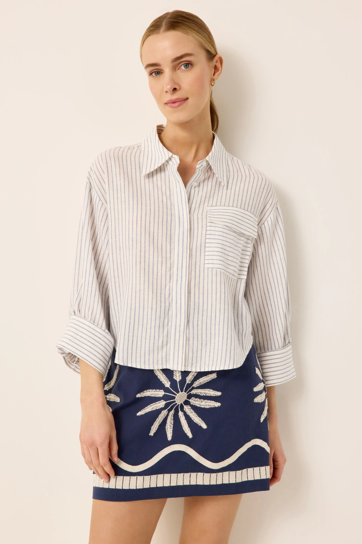 Woman wearing a striped shirt and navy skirt with white patterns against a beige background