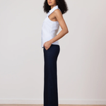 Woman wearing a white blouse and dark pants standing against a plain background