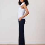 Woman wearing a white blouse and dark pants standing against a plain background