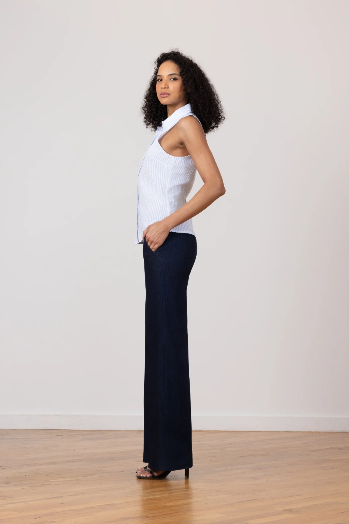 Woman wearing a white blouse and dark pants standing against a plain background
