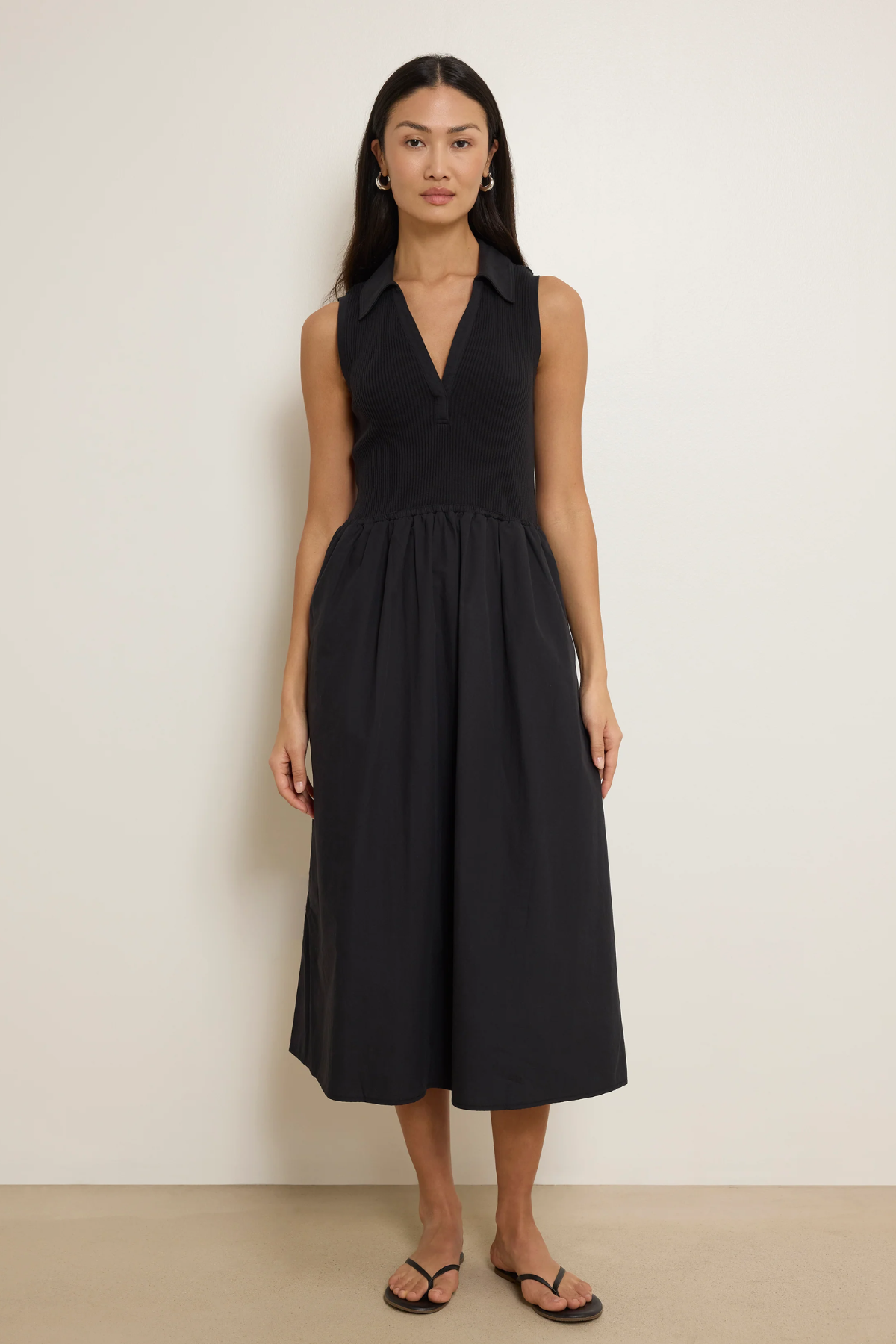 Woman wearing a black sleeveless dress against a plain background