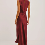 A woman modeling a sleeveless, floor-length burgundy satin dress from the back, featuring a small keyhole cutout at the upper back, set against a plain white studio background.