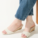 White sandals worn with rolled-up blue jeans on a light background