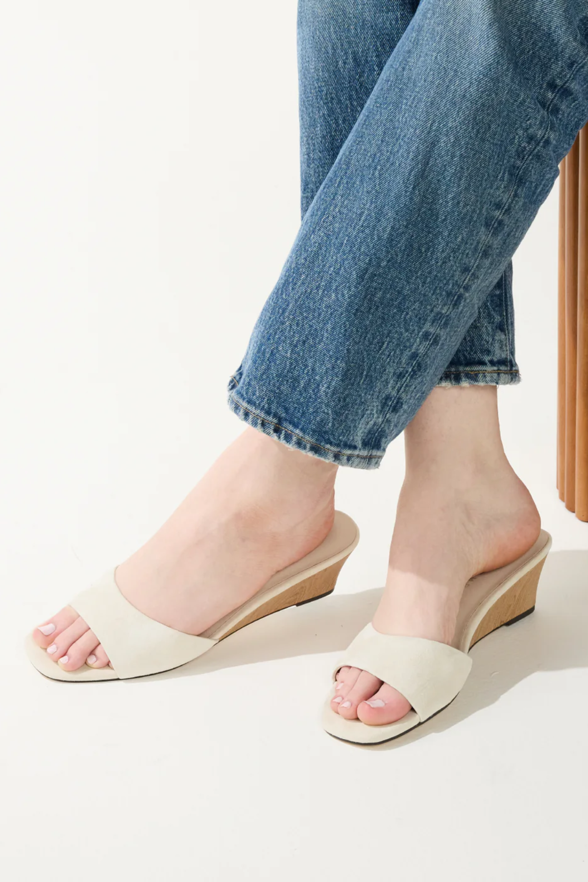 White sandals worn with rolled-up blue jeans on a light background