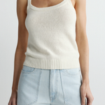 Person wearing a cream-colored tank top and light blue jeans on a plain background