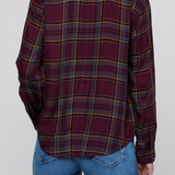 A person shown from the back wearing a long-sleeve plaid button-up shirt in deep burgundy with yellow, blue, and green stripes, paired with blue jeans, against a solid gray background.