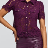 A woman shown from the back wearing a deep purple lace short-sleeve blouse and a matching purple faux-leather skirt against a light gray studio background.